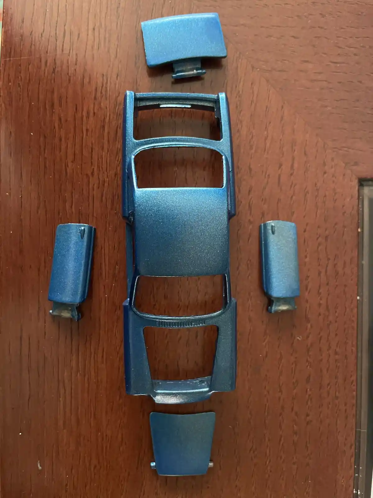 A disassembled blue watch case and its components are laid out on a wooden surface, visually resembling a car chassis with…