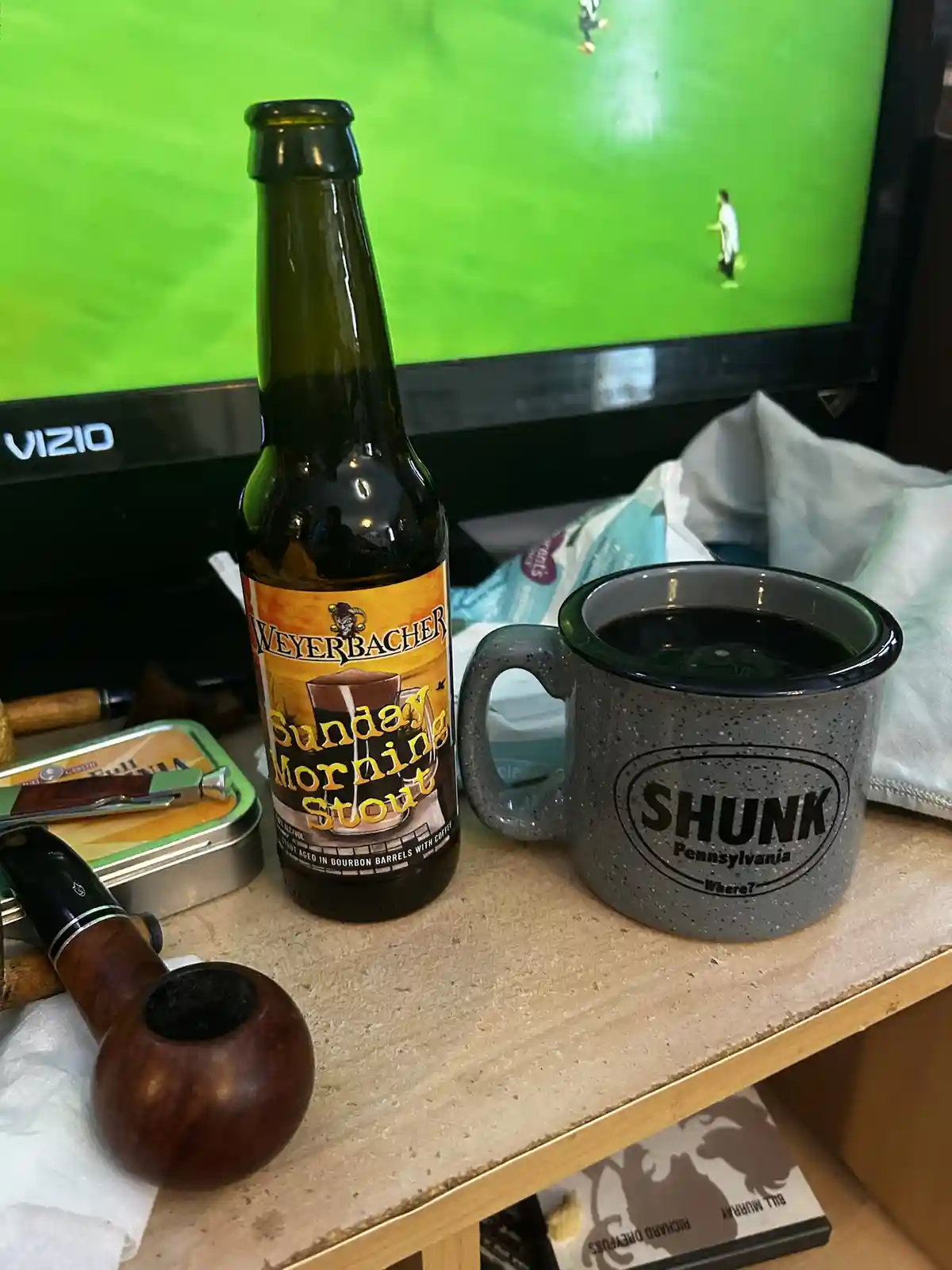 A bottle of Weyerbacher Sunday Morning Stout beer and a gray speckled mug labeled 'SHUNK Pennsylvania Where?' sit on a…