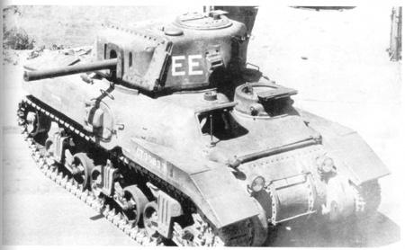 A black-and-white photo of a vintage military tank, likely from World War II, with the letters 'EE' painted in large white…