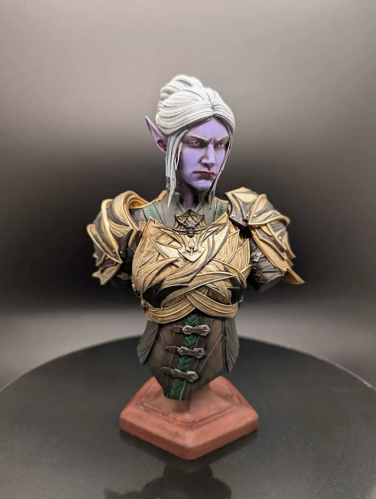 A detailed bust of a fantasy elf character with purple skin, white hair, and pointed ears, wearing ornate gold and green…