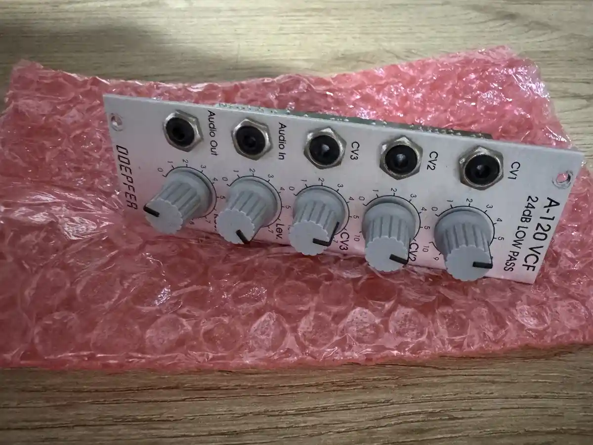 A close-up photo of a Doepfer A-120 VCF analog synthesizer module resting on pink bubble wrap, showing its knobs and jacks…