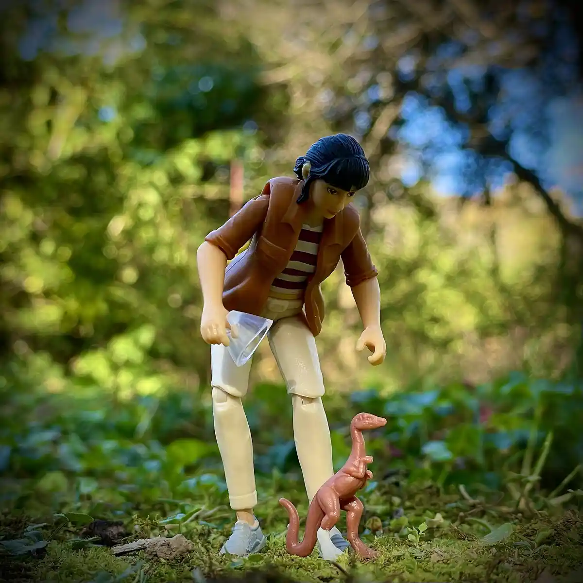 A plastic action figure of a person with dark hair, wearing a brown jacket over a striped shirt and beige pants, is crouched…