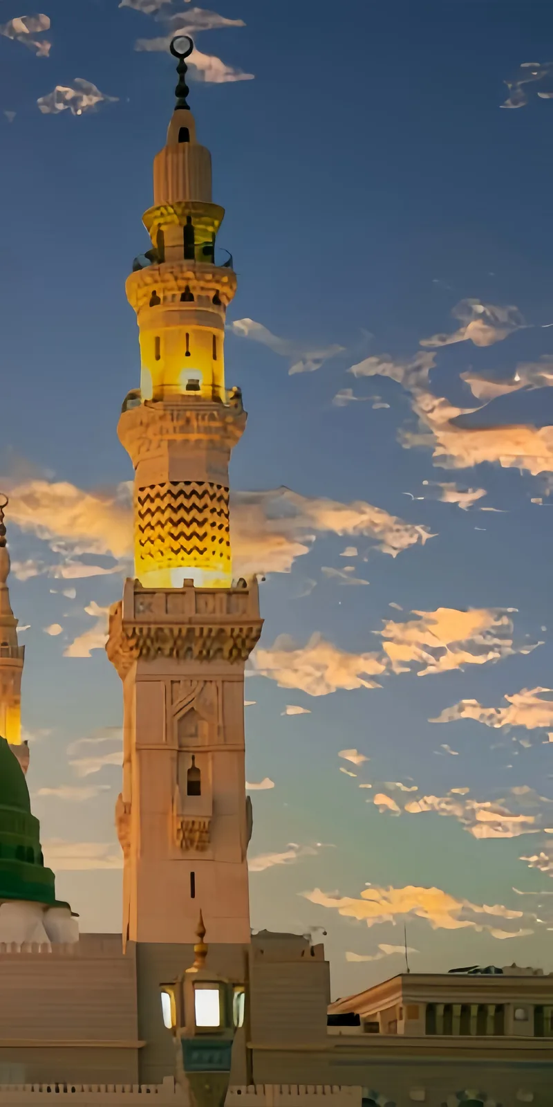 A tall, ornate mosque minaret is illuminated in golden light against a twilight sky with scattered clouds. The structure…