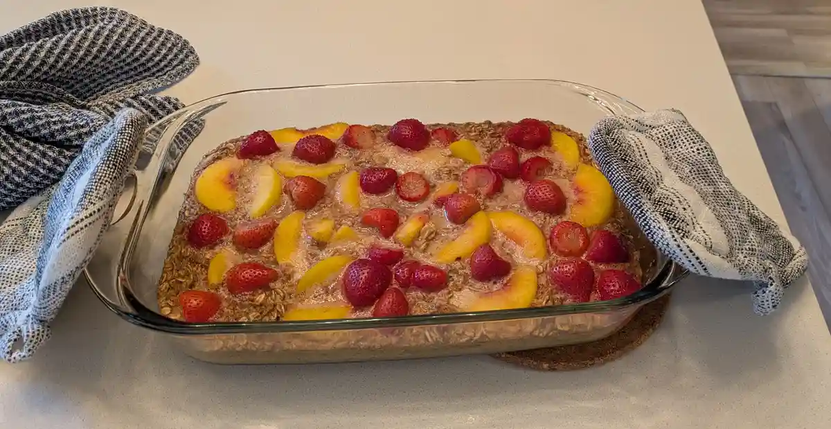 A rectangular glass baking dish sits on a white countertop, filled with a baked oatmeal or casserole topped with sliced…