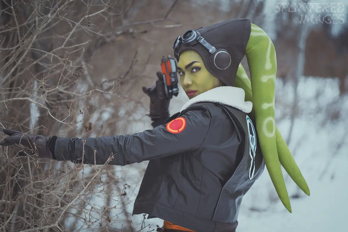 A person in a detailed cosplay of the Star Wars character Hera Syndulla, with green skin, goggles, and a black jacket…