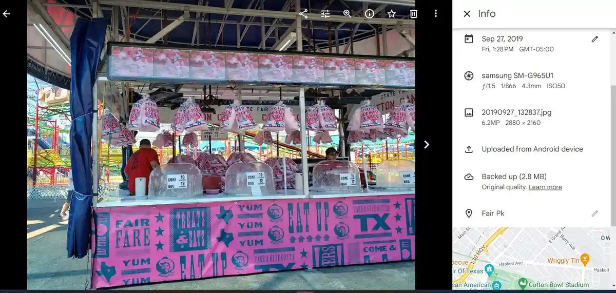 A photo of a pink cotton candy stand at a fair with multiple hanging bags of cotton candy and workers behind the counter…