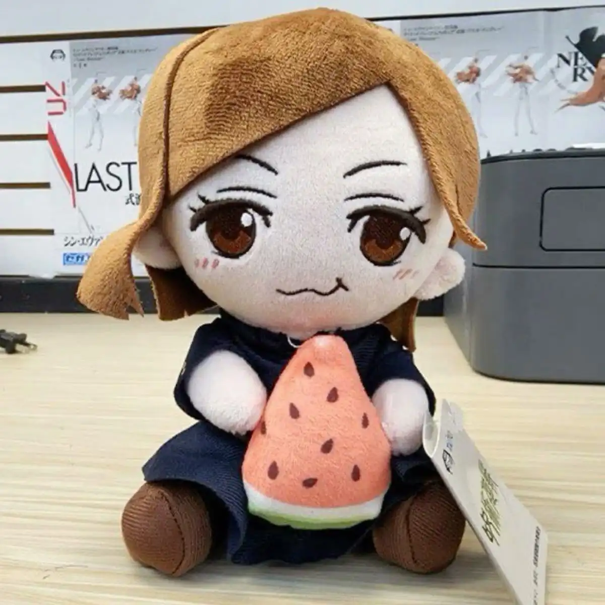 A plush doll with brown hair and large brown eyes sits on a wooden surface holding a plush watermelon. The doll wears a dark…