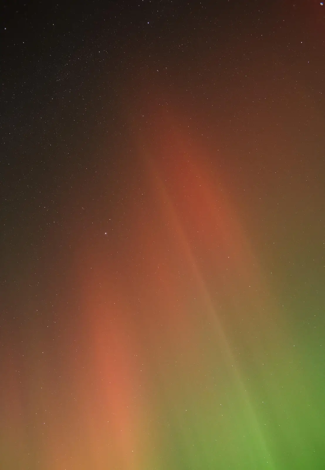 A photograph of the aurora borealis, showing vibrant green and orange ribbons of light streaking across a starry night sky…