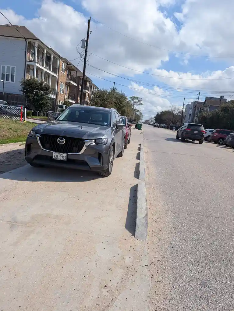A gray Mazda SUV is parked on a concrete driveway next to a street, with its front bumper aligned flush against a concrete…