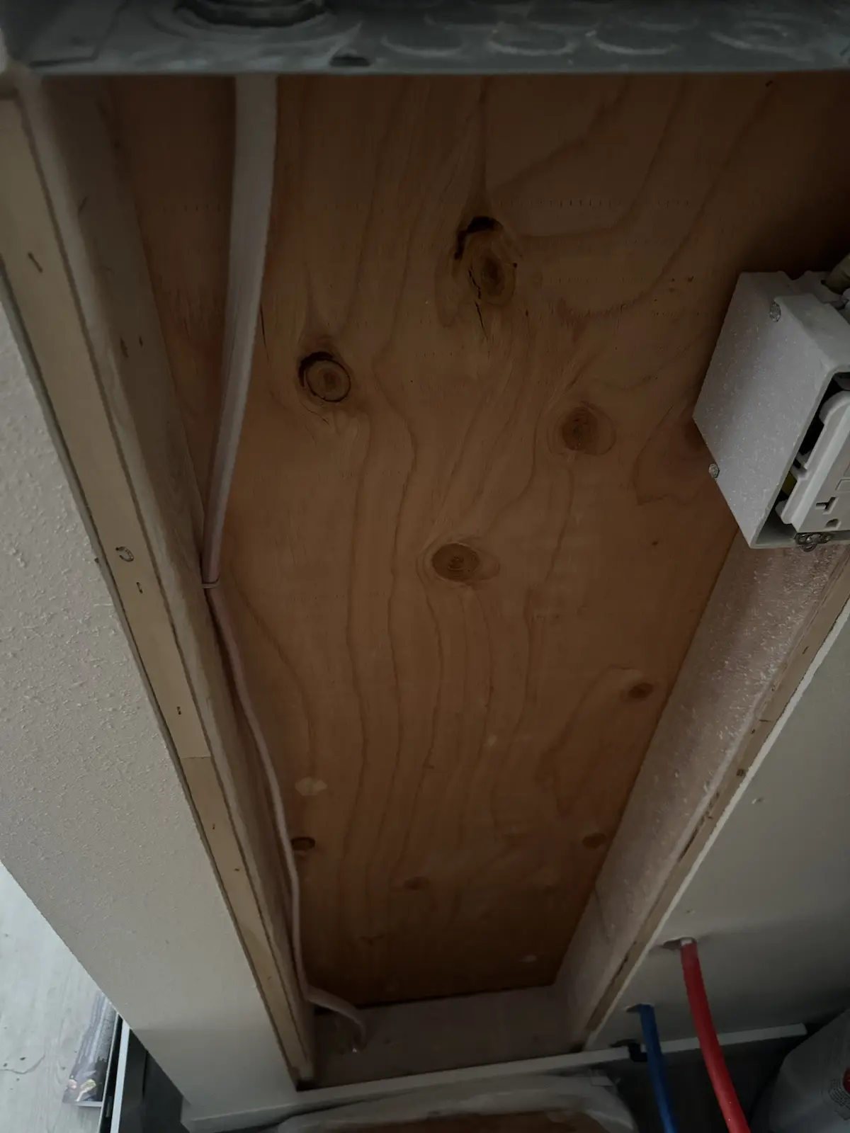 A close-up photo shows the underside of a cabinet or appliance, revealing unfinished plywood with visible wood grain and…
