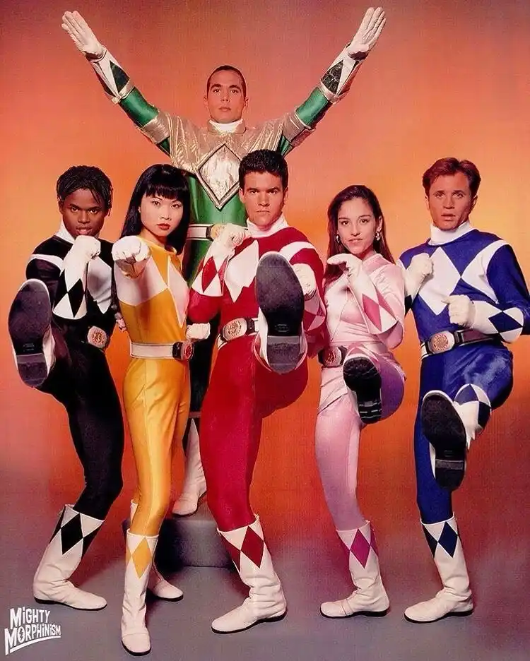 A promotional photo of the Mighty Morphin Power Rangers, five heroes in colorful, diamond-patterned suits (black, yellow…