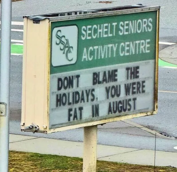 A green and white sign for the 'SECHELT SENIORS ACTIVITY CENTRE' with a marquee board below displaying the text 'DON'T BLAME…