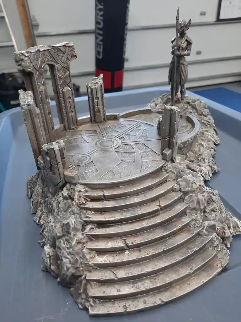 A detailed miniature diorama of a fantasy ruin with stone steps, a circular platform with geometric carvings, and a small…