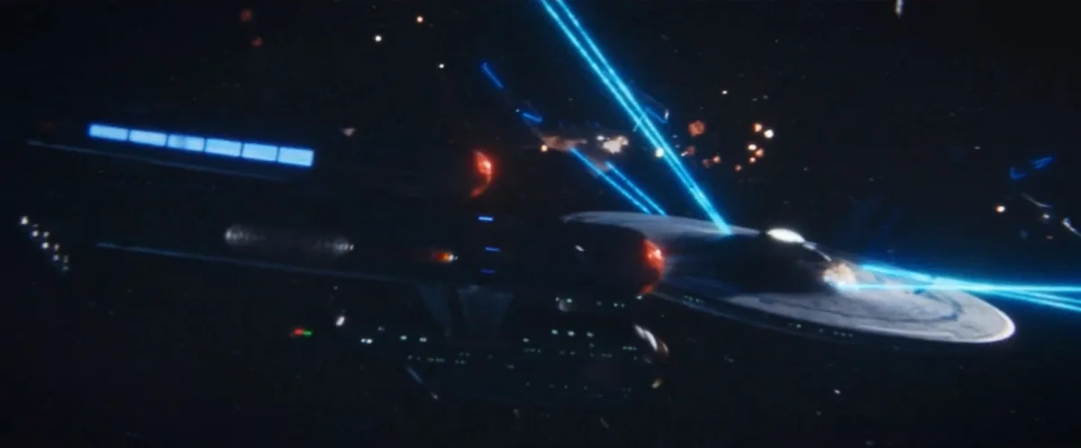 A Starfleet starship, resembling the USS Enterprise from Star Trek, is shown in space firing blue energy beams from its…