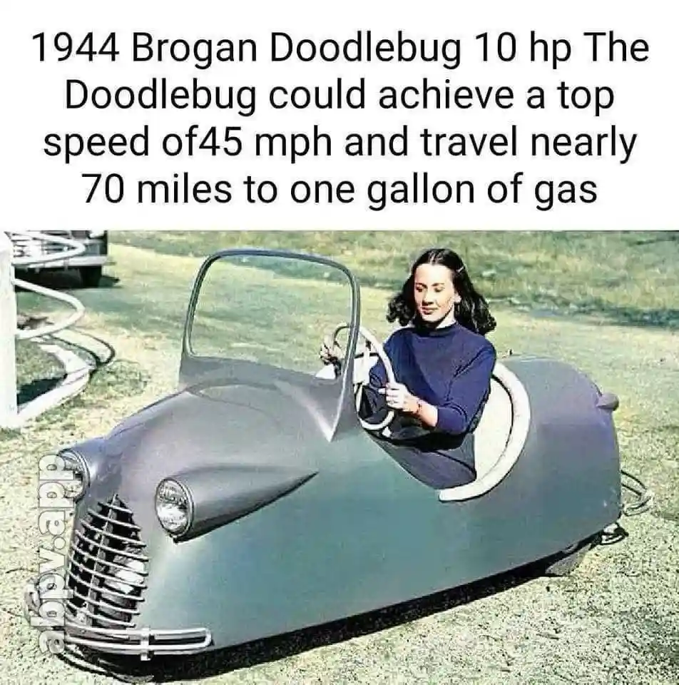 A vintage photograph shows a woman in a dark blue sweater sitting inside a small, gray, 1944 Brogan Doodlebug car, holding…