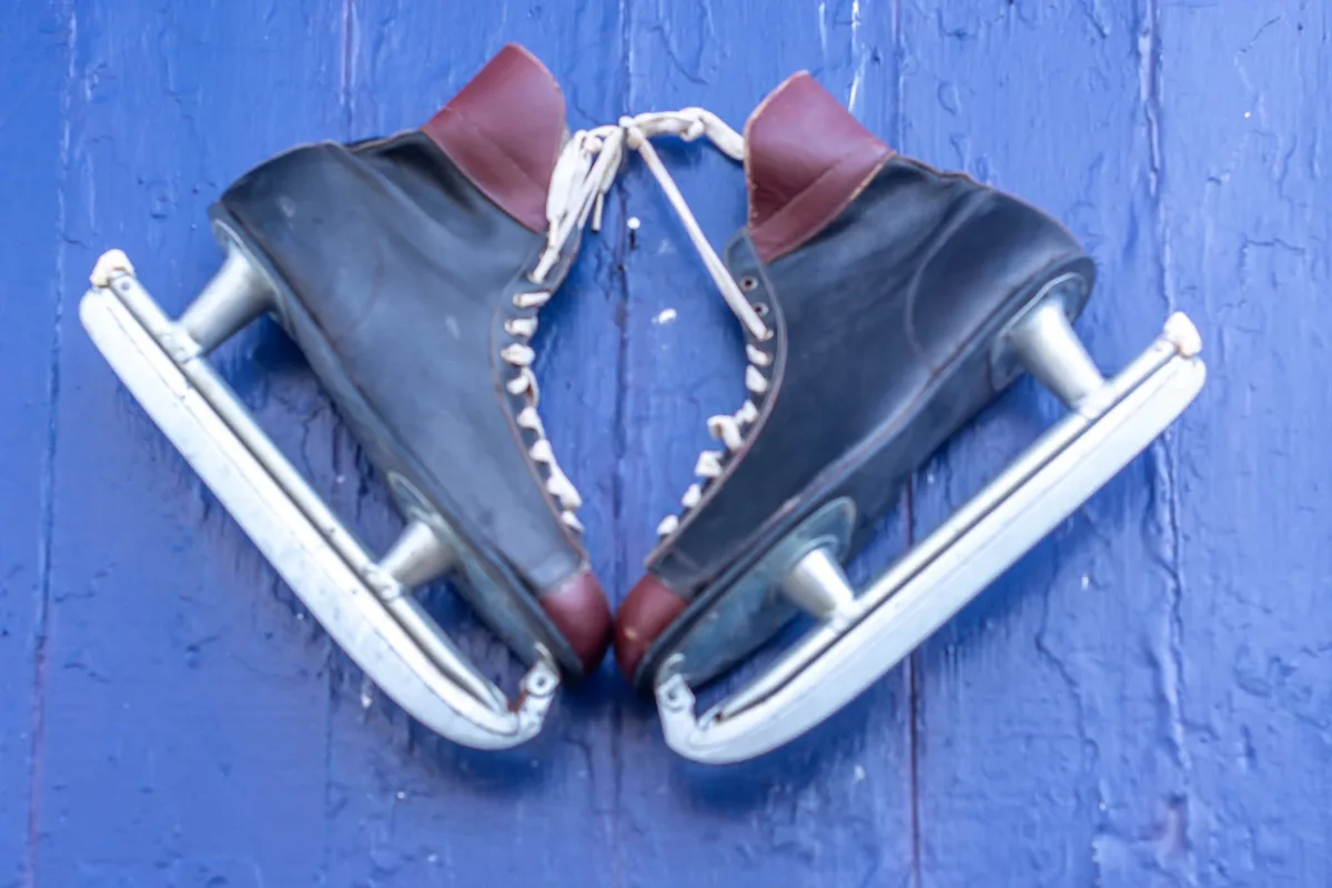 A pair of vintage black leather ice skates with red accents and white laces are arranged in a heart shape against a textured…