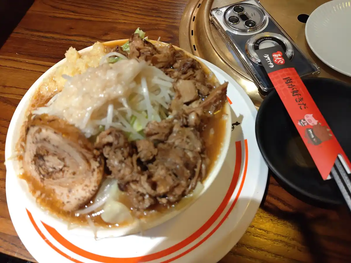 A close-up photo of a steaming bowl of ramen with rich broth, sliced pork, shredded cabbage, and bean sprouts, served on a…