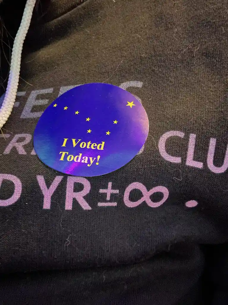 A close-up of a dark hoodie with faded purple text partially visible, featuring a circular blue and purple holographic…