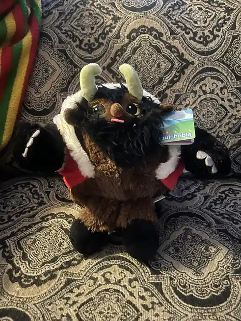 A brown, furry plush toy resembling a Viking or troll with light green horns, a black beard, and a red and white Santa-style…