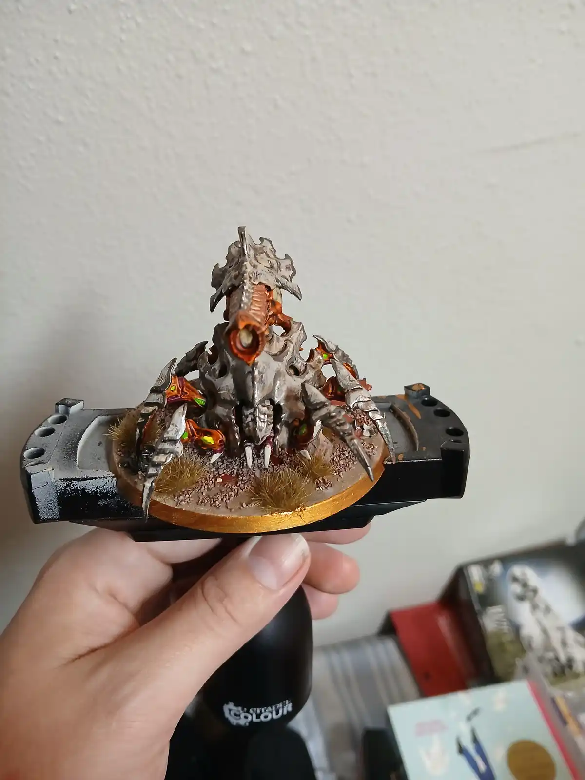 A hand holds a highly detailed, painted miniature of a monstrous, skeletal creature with glowing orange eyes and sharp…