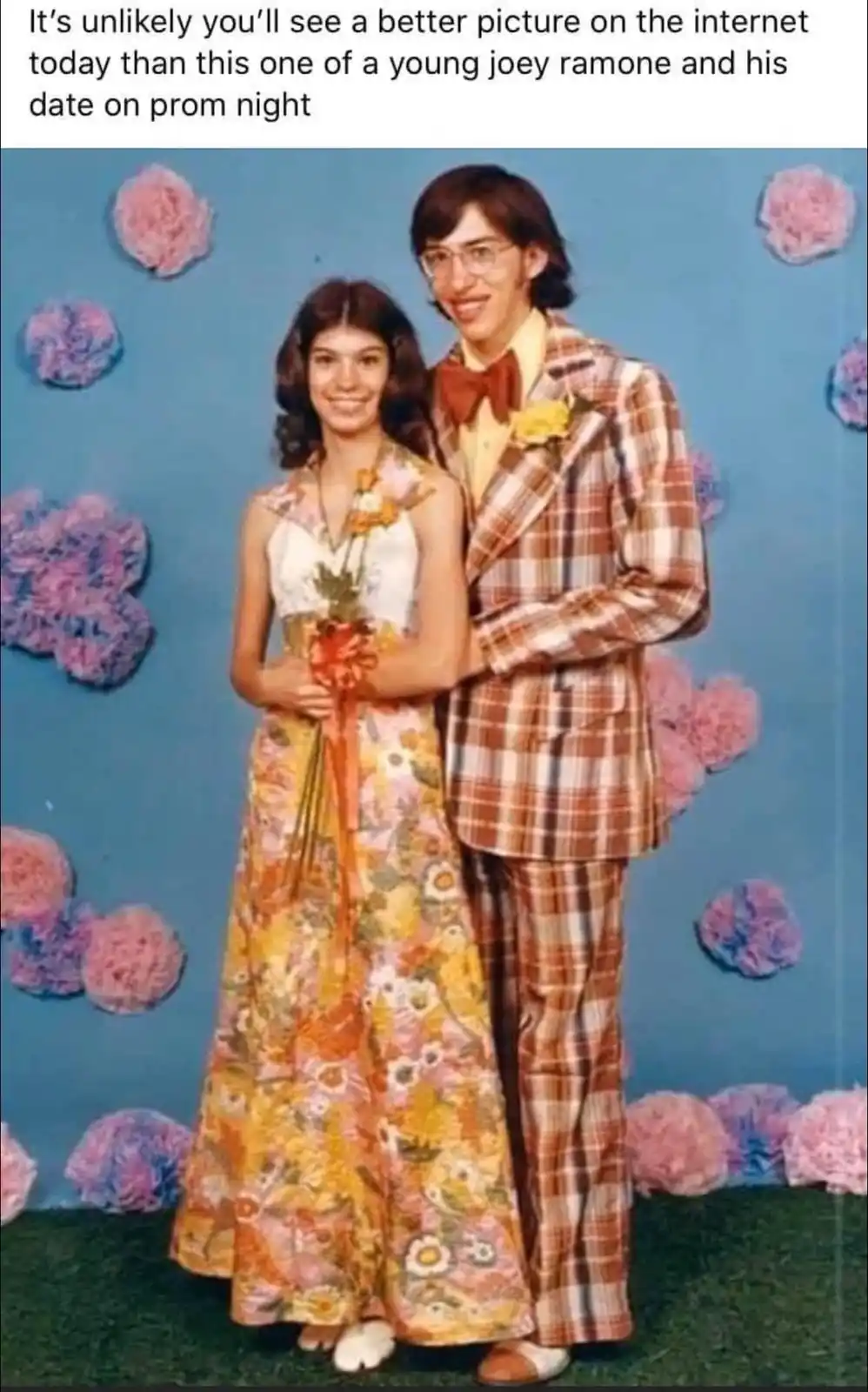 A vintage prom photo shows a young man in a brown plaid suit with a red bowtie and glasses standing next to a young woman in…