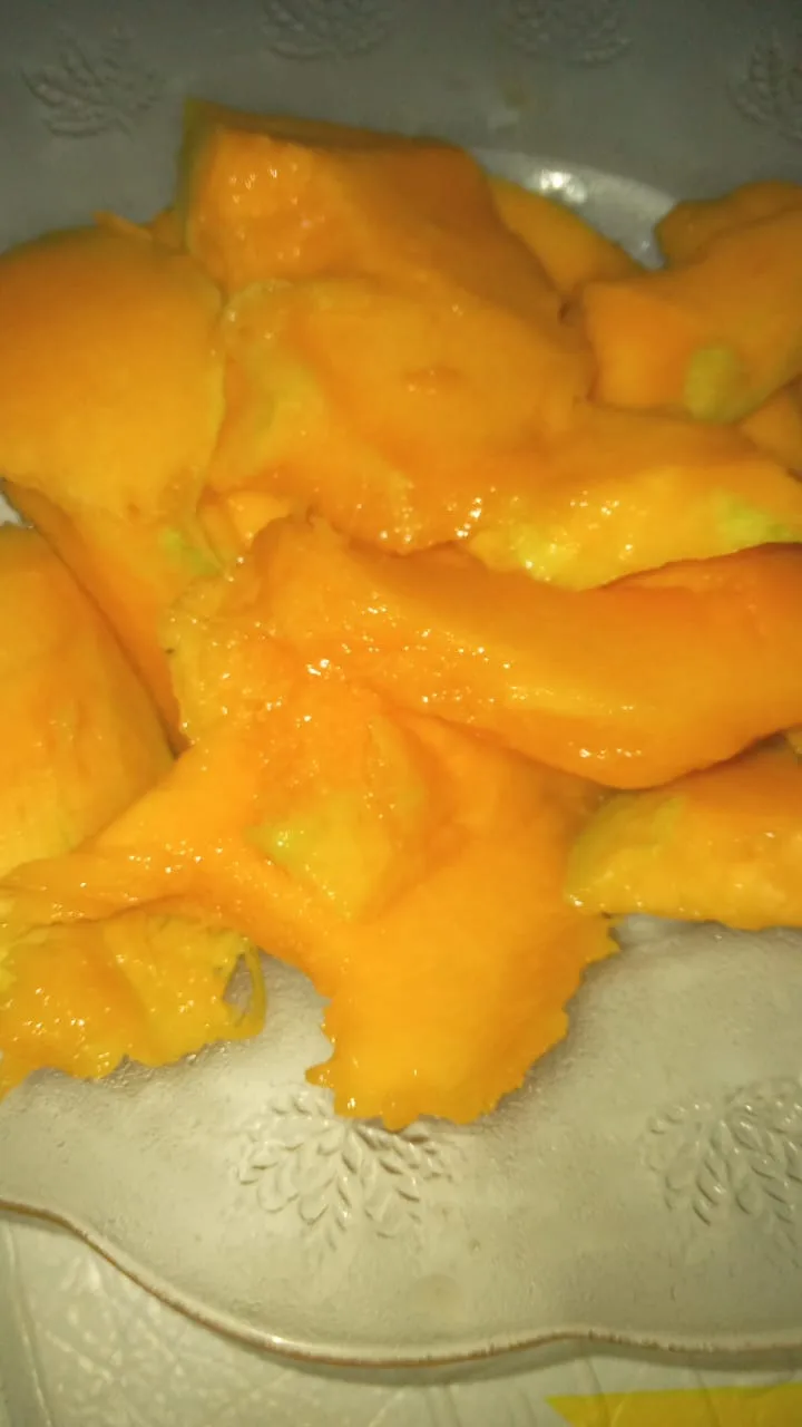 A close-up photo shows a white ceramic plate with embossed leaf patterns, piled high with juicy, bright orange mango slices…