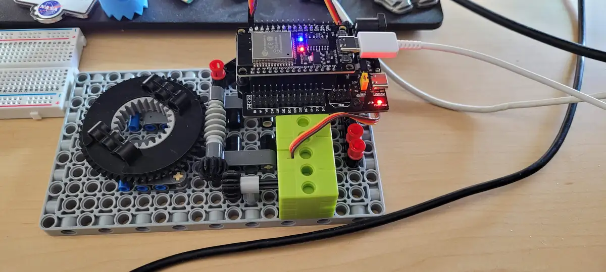 A close-up photo shows a small electronic circuit board, likely an Arduino, mounted on a gray LEGO baseplate with various…
