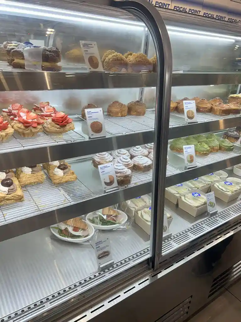 A glass display case at a bakery called 'FOCAL POINT' shows multiple shelves of pastries including strawberry tarts, plain…