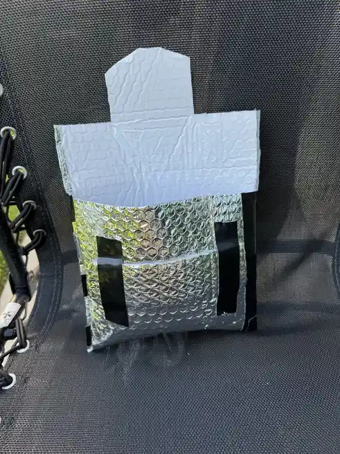 A handmade, box-like structure made from bubble wrap and duct tape is taped to a black mesh outdoor chair. The top is a…