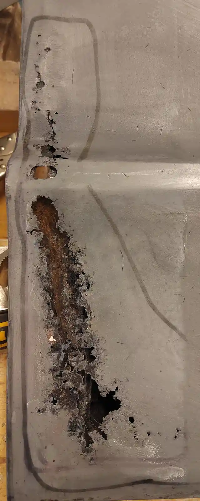 A close-up photo shows a heavily corroded section of a metal car panel, with a long vertical strip of rust and flaking…