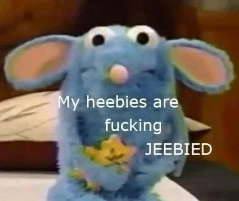 A blue, plush, mouse-like puppet with large ears and a pink nose sits on a bed, looking slightly distressed. White text…