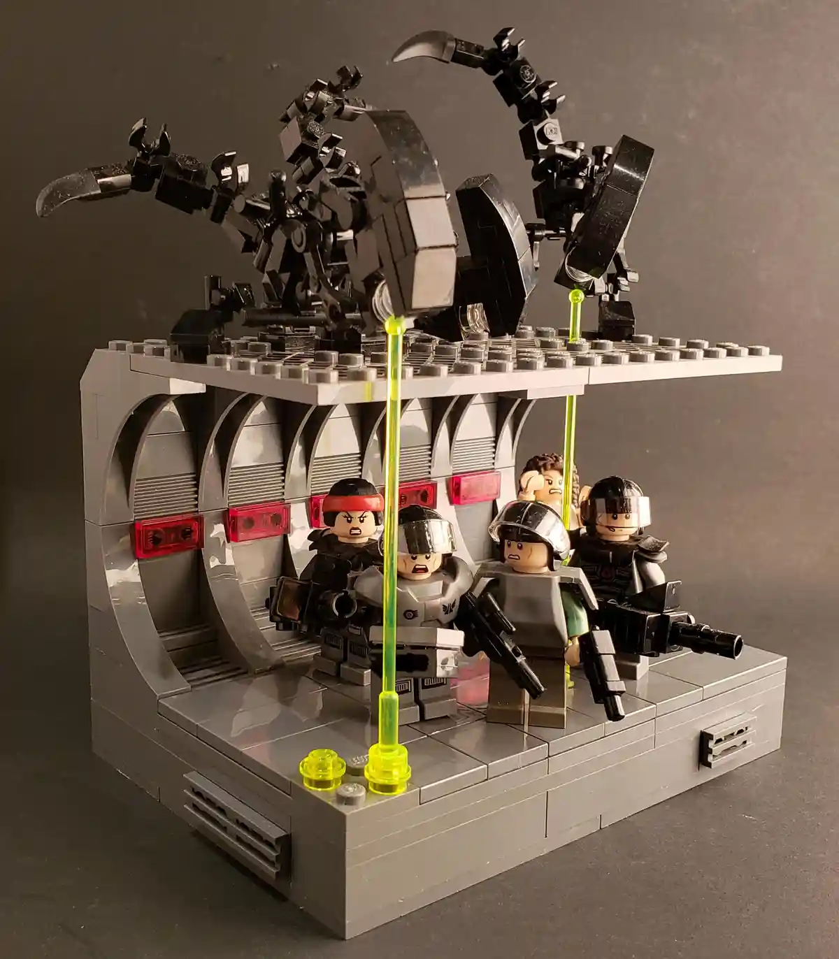 A Lego diorama depicts a sci-fi battle scene with several Lego minifigures in armor holding weapons, facing a large black…