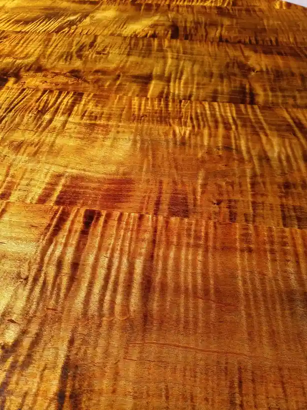 This image shows a close-up of a highly polished wooden surface with rich golden-brown tones and intricate, flowing grain…