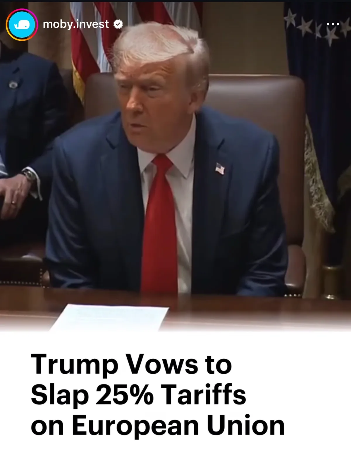 A still image of Donald Trump seated at a wooden desk in a formal setting, wearing a dark blue suit, white shirt, and red…
