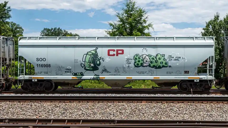 A silver Canadian Pacific (CP) freight train car, numbered SOO 116908, is covered in colorful graffiti art including a green…