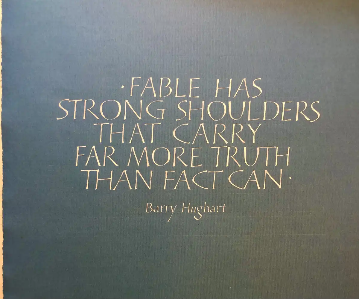 A close-up of a dark blue textured book cover or plaque with gold embossed text. The text reads: 'FABLE HAS STRONG SHOULDERS…