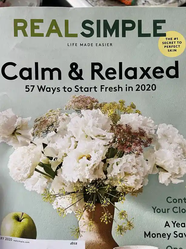 The cover of a Real Simple magazine from January 2020 features a vase of white and yellow flowers and a green apple against…