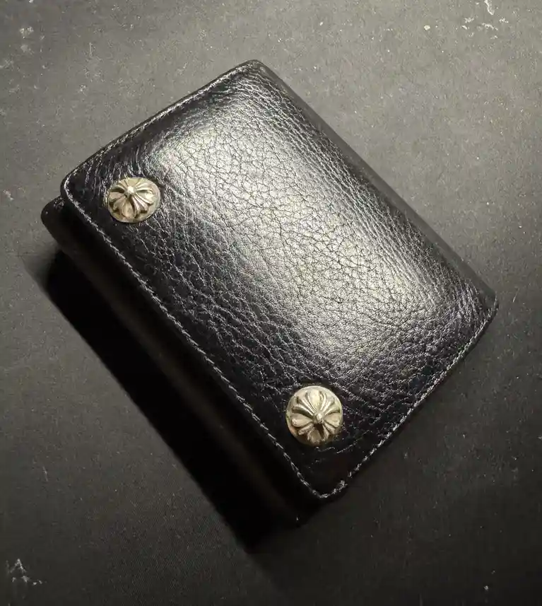 A close-up photo of a black leather wallet with two ornate silver conchos on its corners, resting on a dark textured…
