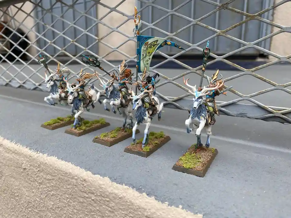 A row of six intricately painted miniature figurines depicts fantasy knights riding white deer with blue manes and antlers…