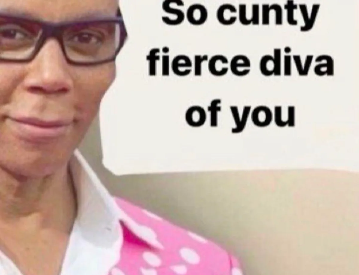 A close-up photo of a woman with dark-rimmed glasses and a slight smirk, wearing a pink polka-dot top over a white collared…
