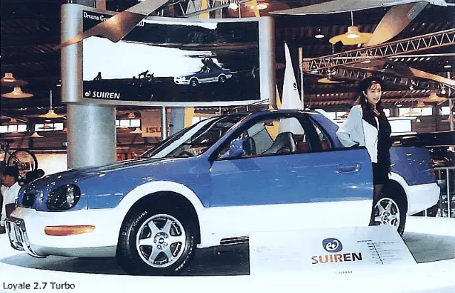 The image displays two identical side-by-side photos of a blue and white Suiren Loyale 2.7 Turbo car at an auto show, with a…