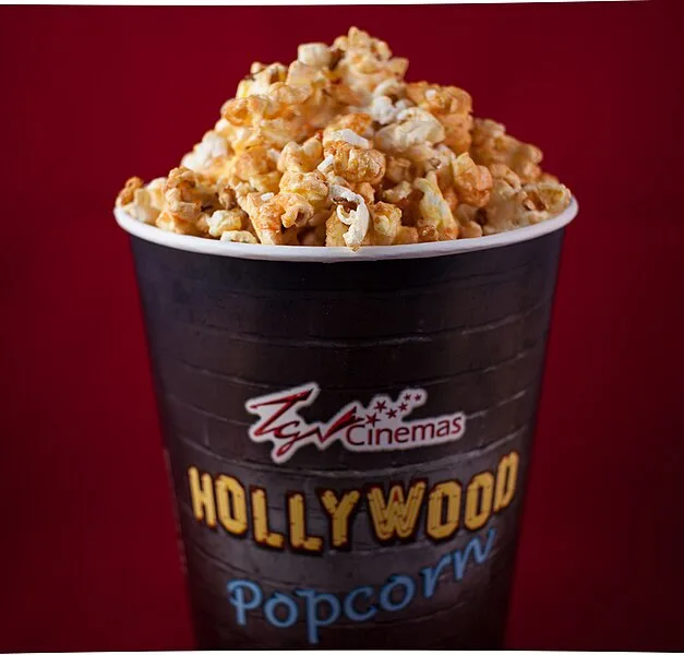 A close-up of a black paper cup overflowing with buttered popcorn, branded with 'TGV Cinemas' and 'HOLLYWOOD Popcorn' in…