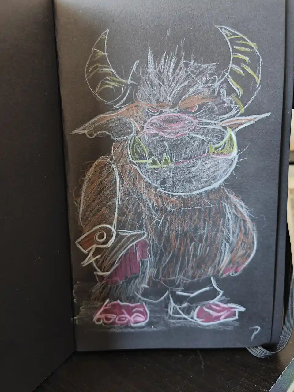 A chalk drawing on dark paper depicts a cartoonish, angry-looking monster with horns, sharp teeth, and a furry body, wearing…