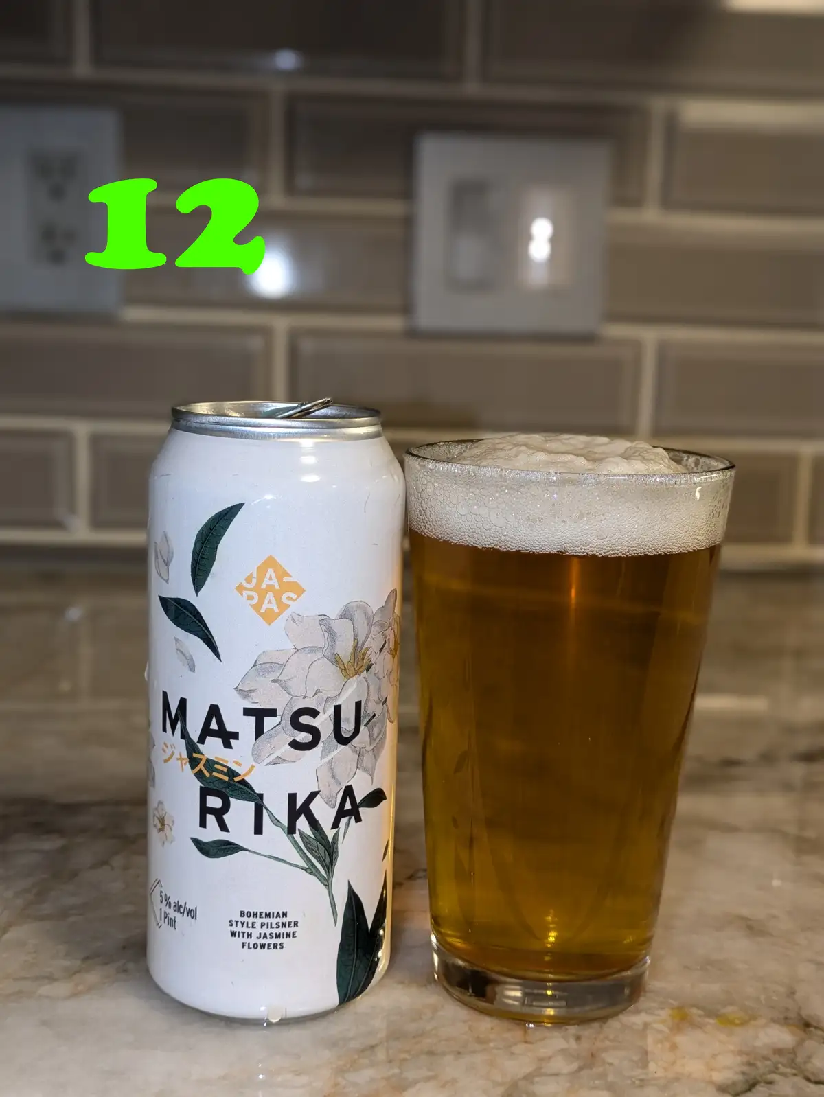 A white can of 'MATSURIKA' beer, labeled as a Bohemian style pilsner with jasmine flowers, sits next to a full glass of the…