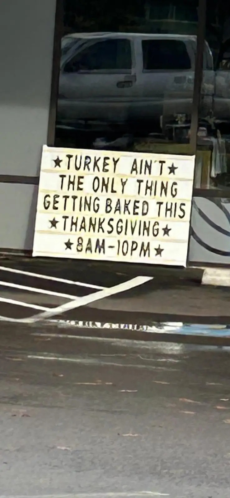A lightbox sign outside a storefront reads '★TURKEY AIN'T★ THE ONLY THING GETTING BAKED THIS ★THANKSGIVING★ ★8AM-10PM★'…