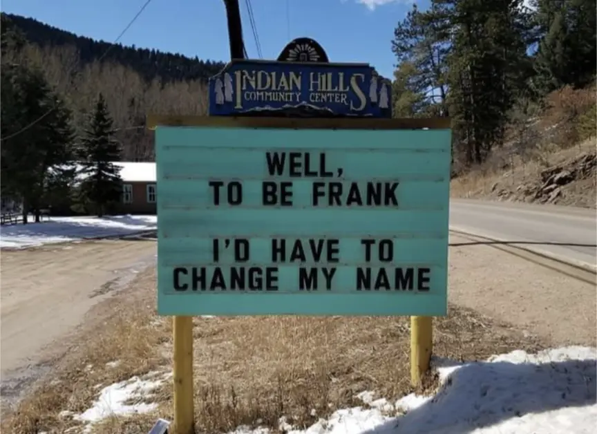 A light blue outdoor marquee sign at the Indian Hills Community Center reads 'WELL, TO BE FRANK I'D HAVE TO CHANGE MY NAME'…