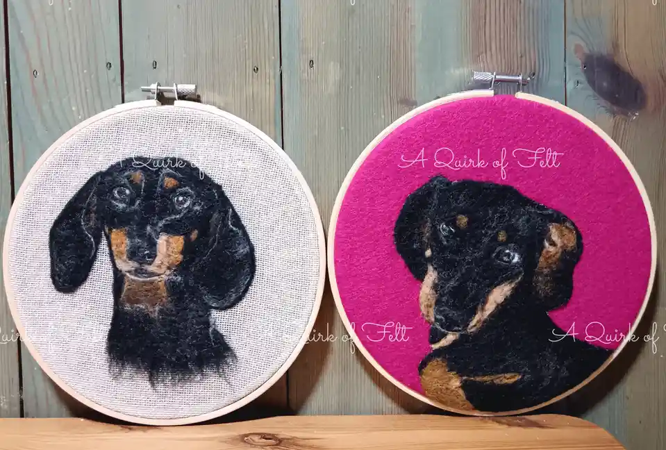 Two felt portraits of a black and tan dachshund are displayed in embroidery hoops, one on white fabric and one on bright…
