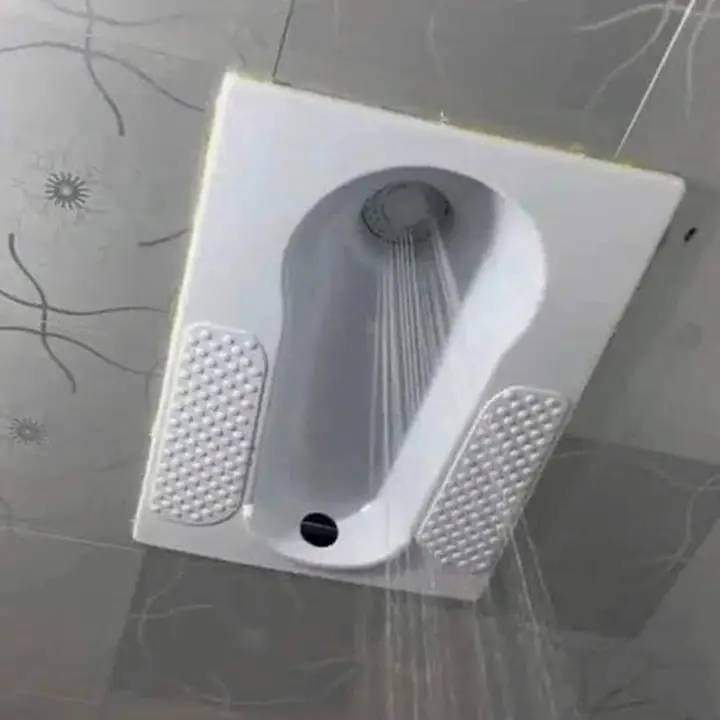 a white ceramic squat toilet is shown mounted on a tiled floor, with water visibly spraying from a showerhead positioned…