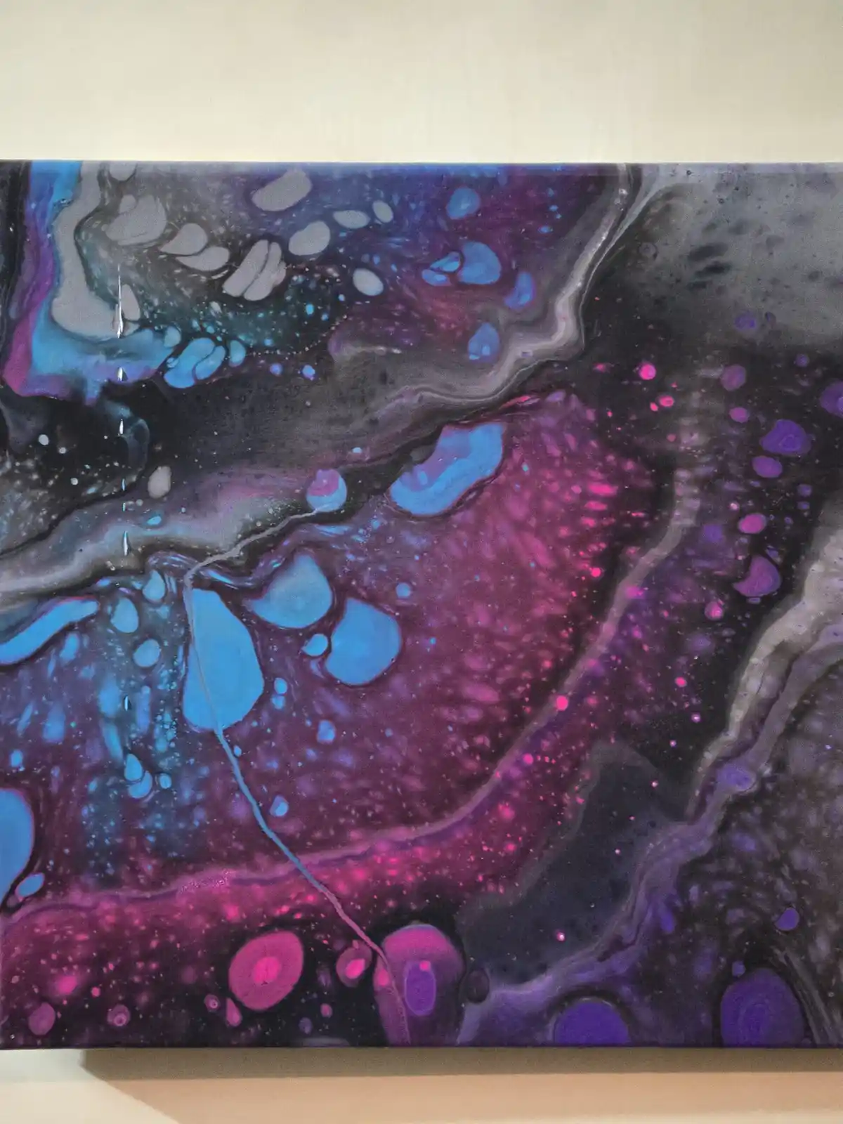 A close-up photo of a vibrant abstract painting with swirling patterns of blue, purple, and magenta against a dark…