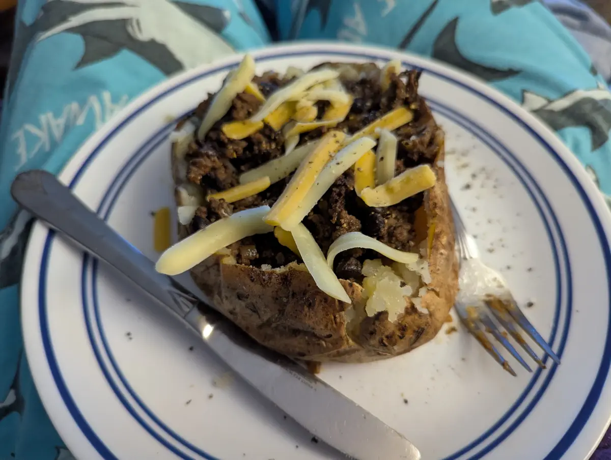 A baked potato split open and filled with seasoned ground meat, black beans, and shredded cheese, served on a white plate…
